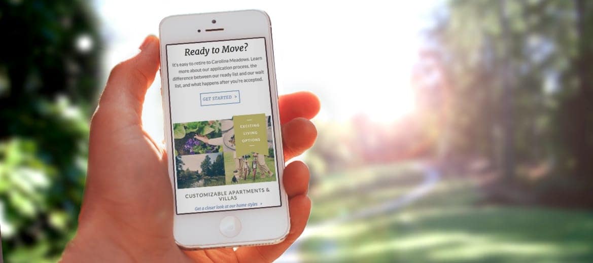 A hand holding a mobile phone showing the Carolina Meadows website